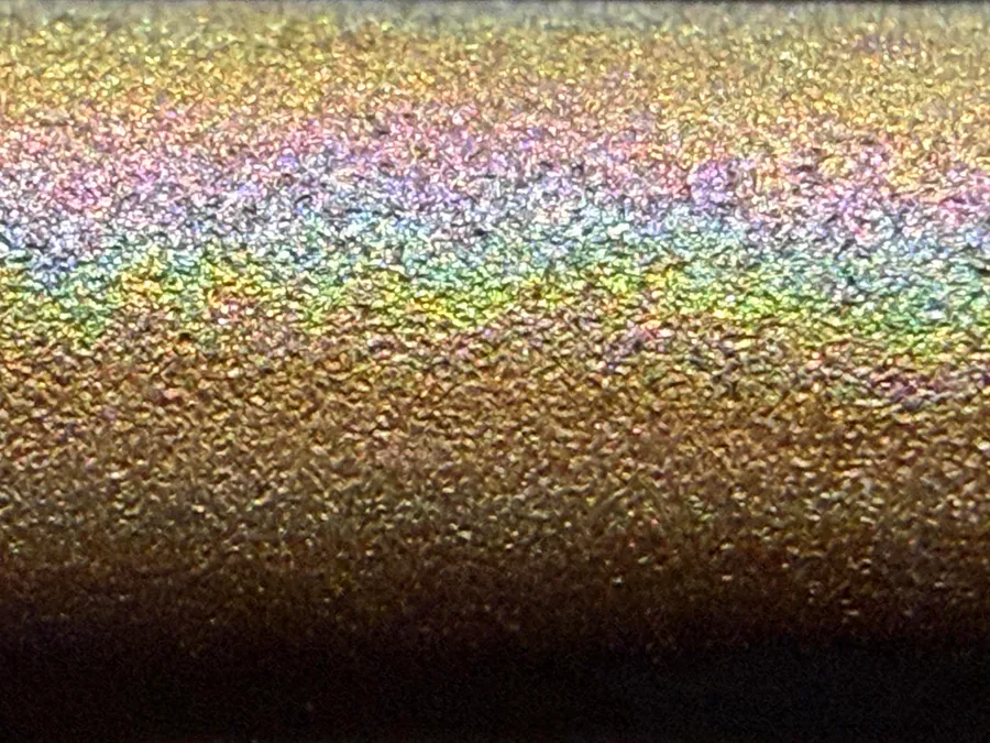 Close-up of a metal electrode rod with a shimmering band of rainbow colours across its surface