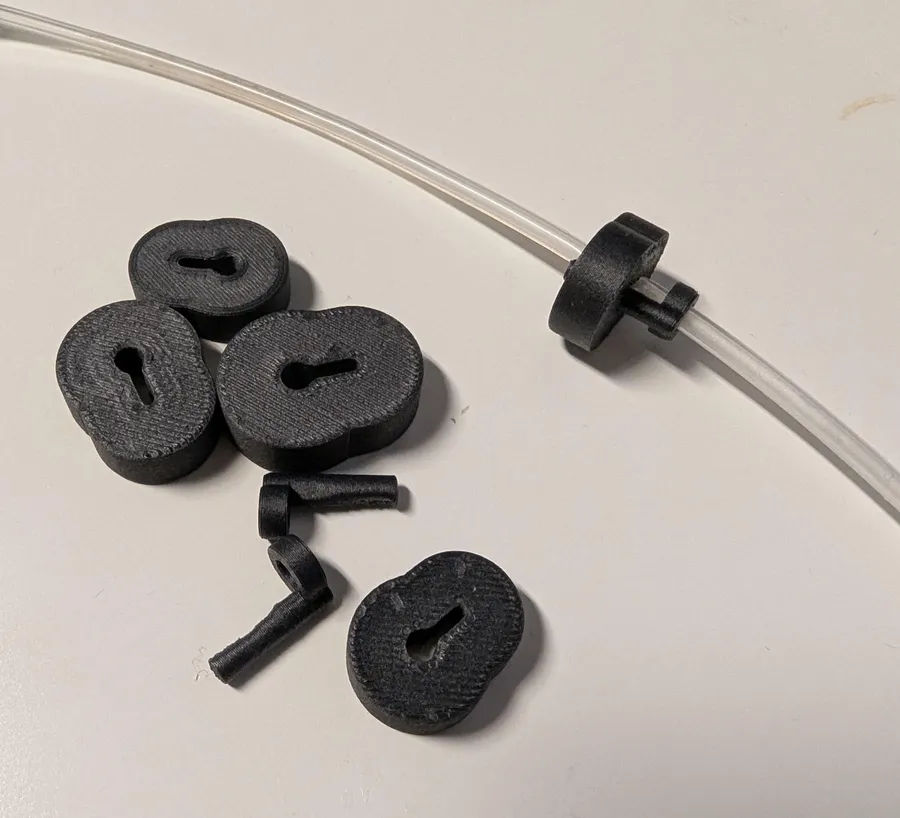 Five small black 3D-printed pinch sliders with keyhole slots, one fitted on a length of clear silicone tubing