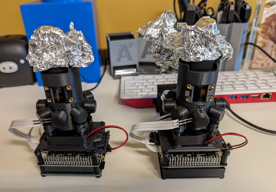 Two Pioreactors standing side by side on a desk, each with a foil-covered vial, one connected to a Raspberry Pi 400 keyboard computer